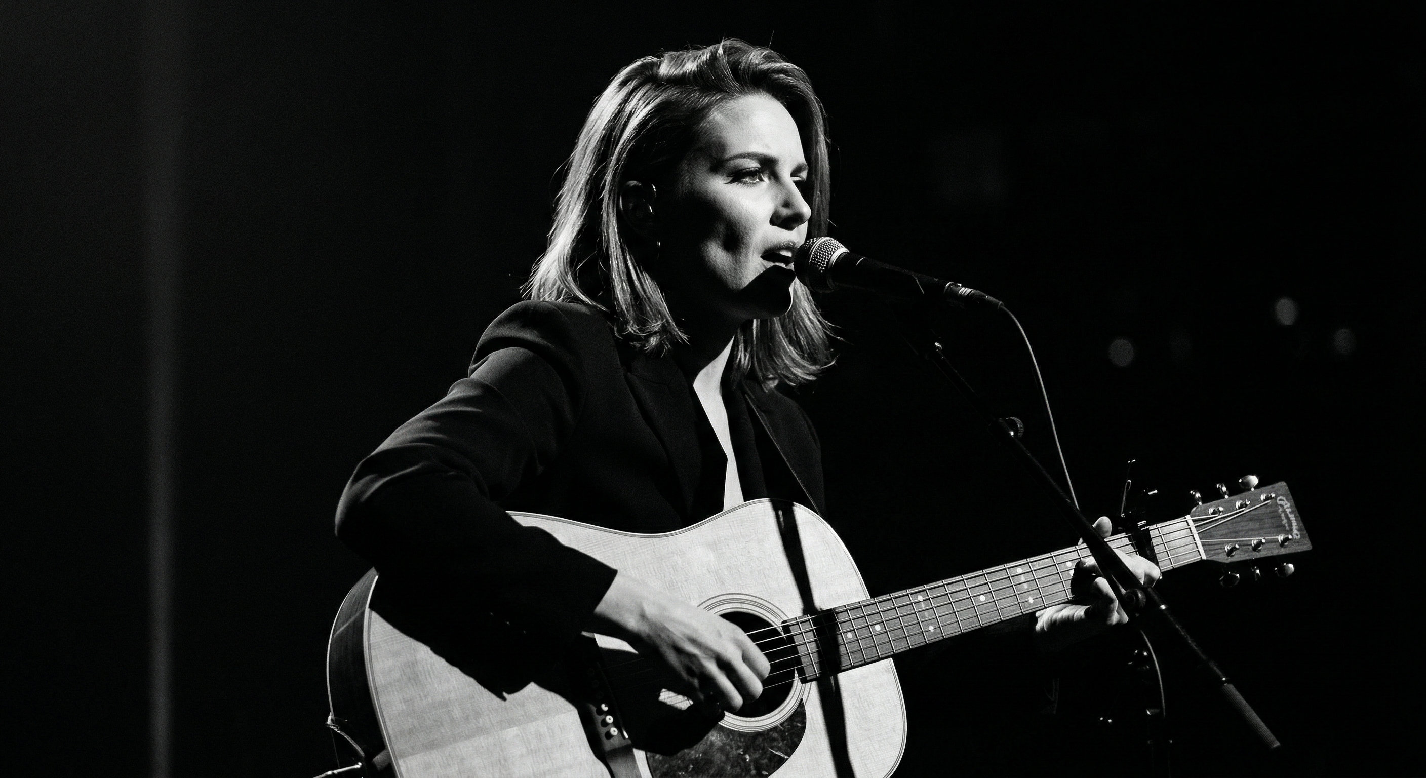 Artist performing live with an acoustic guitar in a starkly lit room